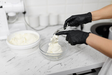 The confectioner puts cream cheese in a glass bowl for making sweets close-up. Cooking concept. Cooking cream for cupcakes.