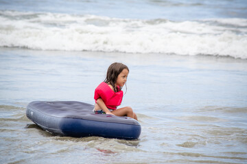 Criança brincando na praia com boia flutuante nas ondas do mar na cor azul e rosa.