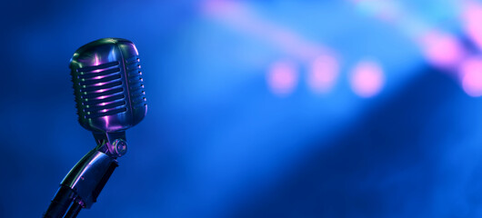 Vintage vocal microphone on concert stage with blue and pinks spotights. Wide panoramic background...