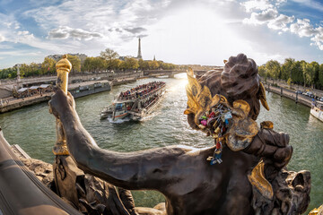 The Pont Alexandre III (bridge) with sculptures against tourist boat on Seine and Eiffel Tower in Paris, France