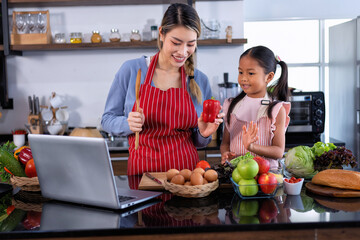 Young mother teach daughter in the kitchen learn online cooking clean food from the laptop computer