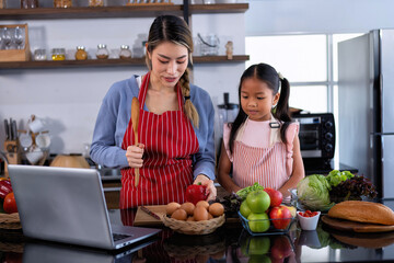 Young mother teach daughter in the kitchen learn online cooking clean food from the laptop computer