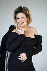 Fototapeta premium A smiling woman in a black suit stands holding a jacket on her shoulders against a white background.