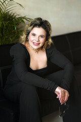 Fototapeta premium A smiling woman in a black suit sits holding glasses.