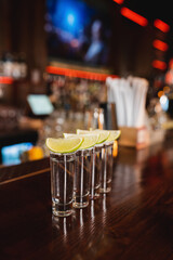 Tequila shots with fresh lime on wooden bar stand.