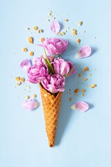 Wafer cone with tulips on blue background. Flower ice cream, spring concept with first flowers, mother's day, top view.