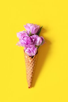 Wafer cone with tulips on yellow background. Flower ice cream, spring concept with first flowers.