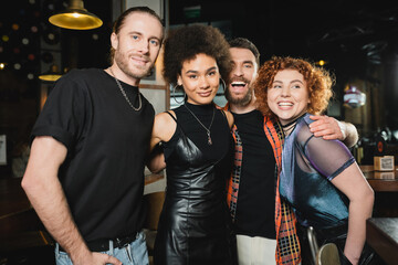 Carefree and excited man hugging interracial friends in bar at night.
