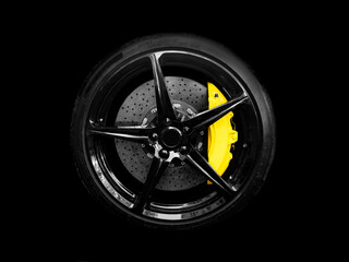 Car alloy wheel and tyre isolated on black background. New alloy wheel with tire and yellow carbon...