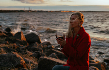 Girl with a glass of wine by the sea at sunset, the wind in her hair