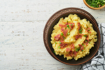 Mashed boiled potatoes. Bacon mashed potatoes with green onion, pepper and cheddar cheese in bowl on light old wooden backgrounds. Delicious creamy mashed potatoes. Top view.