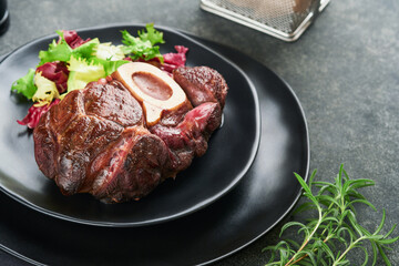 Steaks Osso Buco. Sliced beef grilled Osso Buco or porterhouse meat steak with garnished with salad and french fries on black marble board on old wooden background. Top view. Mock up.