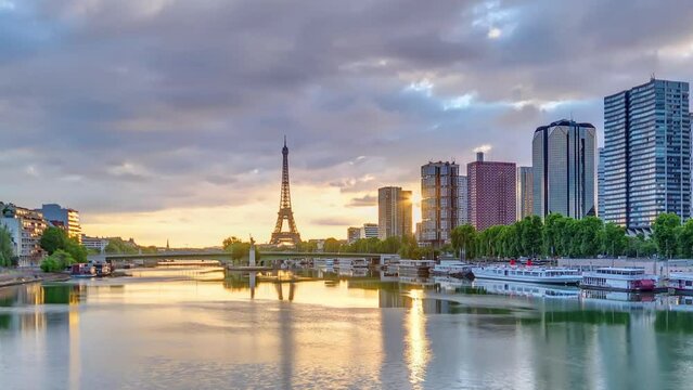 Eiffel Tower sunrise timelapse with boats on Seine river and in Paris, France. Aerial view from Mirabeau bridge with dramatic sky. Modern buildings and traffic on a road. The Statue of Liberty