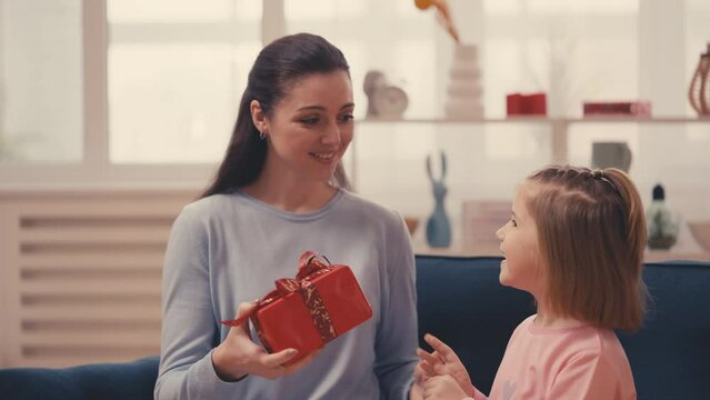 Little girl runs to her mom, presenting a red gift box, celebrating Mother's Day