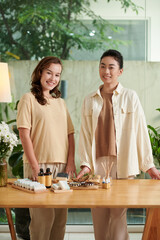 Portrait of happy businesswomen standing at table with handmade organic cosmetics