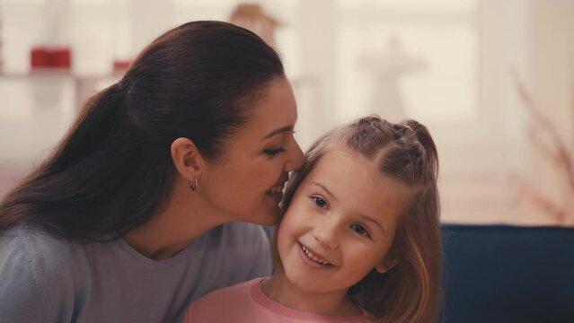 Cheerful mother tells secrets to her little daughter, happy parenting and family