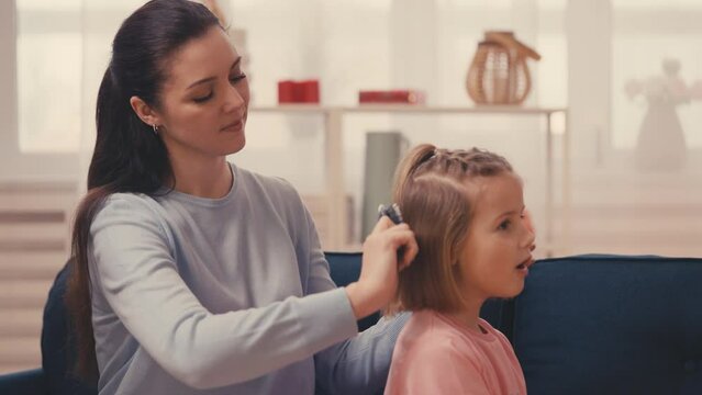 Caring young mother combing little daughter's hair, happy motherhood, family