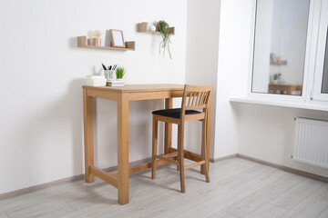 Comfortable workplace with wooden desk near white wall at home