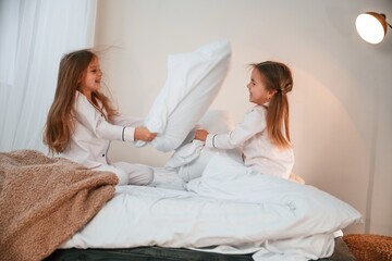 On the bed. Pillow fight. Two little girls are playing and having fun together in domestic room
