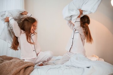 On the bed. Pillow fight. Two little girls are playing and having fun together in domestic room