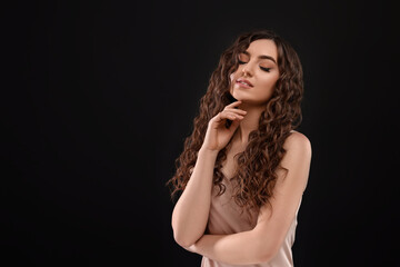 Beautiful young woman with long curly brown hair on black background, space for text