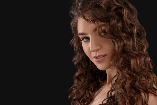 Beautiful young woman with long curly brown hair on black background, closeup. Space for text