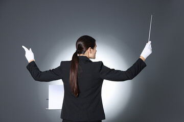 Professional conductor with baton and note stand on grey background, back view