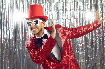 Young positive african american showman in shiny suit having fun on silver background with sparkle...