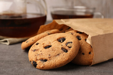 Paper bag with delicious chocolate chip cookies and tea on grey table, closeup