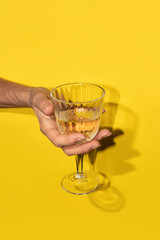 Hand holding the white wine in a  glass on a yellow background