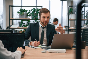 Man in suit is working in the office by laptop. With woman that siting by the table