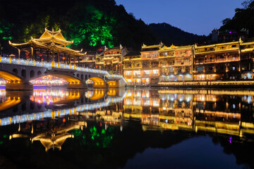 Chinese tourist attraction destination - Feng Huang Ancient Town (Phoenix Ancient Town) on Tuo Jiang River with bridge illuminated at night. Hunan Province, China