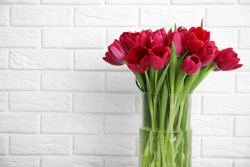 Bouquet of beautiful tulips in glass vase near white brick wall. Space for text