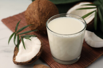 Glass of delicious vegan milk, coconut pieces and palm leaves on white marble table
