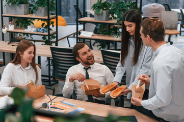 Having a conversation. Group of coworkers are eating food from eco boxes in the office together