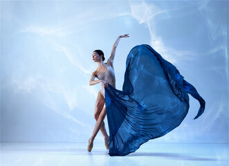 One adorable ballerina wearing beige bodysuits emotional dancing with fabric silk over blue background © Lustre Art Group 