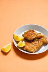 Classic fried Wiener Schnitzel served with lemon on a white plate. Breaded fried meat. A traditional dish of Austrian or German cuisine. Close-up. Copy space. Orange bright background