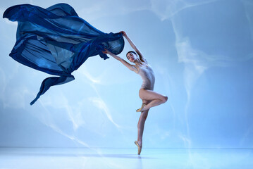 Charming ballerina posing with silk fabric over blue background. Concept of classic ballet, inspiration © Lustre Art Group 