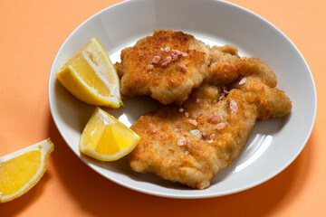 Classic fried Wiener Schnitzel served with lemon on a white plate. Breaded fried meat. A traditional dish of Austrian or German cuisine. Close-up. Copy space. Orange bright background