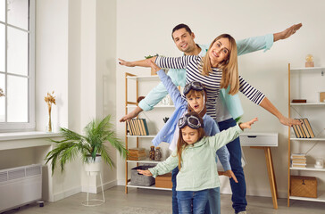 Fototapeta na wymiar Happy young family playing together imitating airplane with hands. Cheerful father, mother and kids spreading their arms as wings pretending flying. Family having fun in living room at home