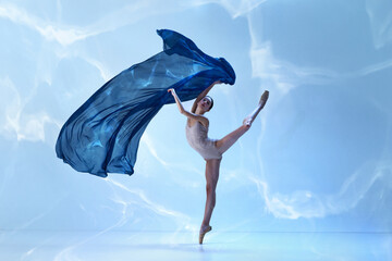 Young and graceful ballet dancer jumping with fabric over blue background. Art, motion, action, flexibility, inspiration concept