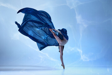 Young classical dancer dancing on fingertips with silk fabric over blue background. Beauty and grace in movements © Lustre Art Group 