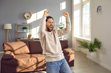 Young happy man raising his arms with fists with joyful face expression like a winner at home....