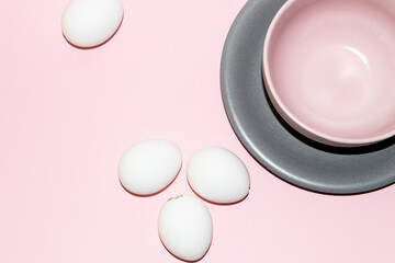 White eggs and a pastel pink bowl on a gray plate over pink background