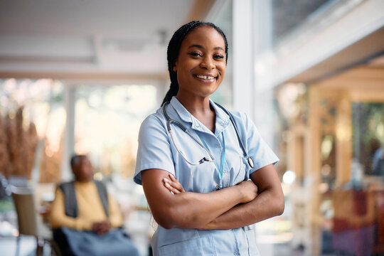 Happy Black Nurse With Arms Crossed In Nursing Home Looking At Camera.