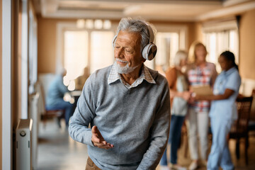 Senior man enjoys in music over headphones in residential care home.