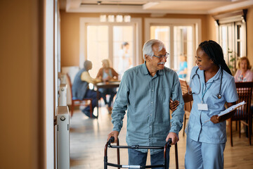 Happy black nurse assists senior man in using mobility walker at nursing home. - Powered by Adobe