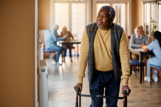 Pensive black senior man with mobility walker by window in nursing home.