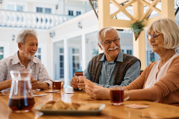 Group of happy senior friends playing cards on patio in nursing home.