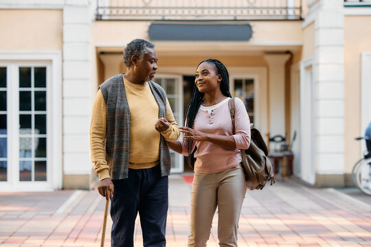 Happy black woman talks to her senior father while vising him in residential care home.